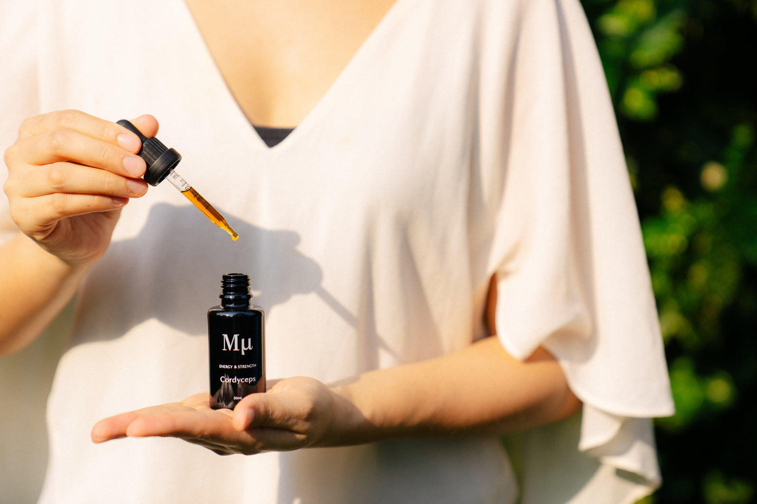 A female holding the Cordyceps extra on her palm with the other hand holding the dropper in a garden