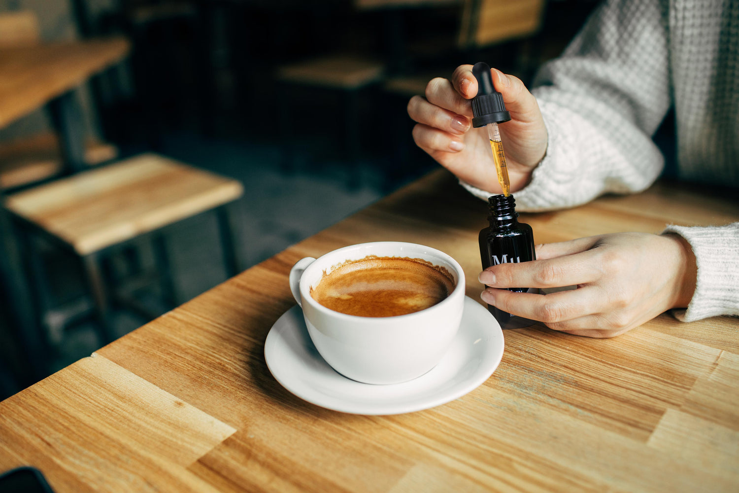 A person holding the Mµ dropper bottle and adding the mushrooms extract to her coffee in a minilistic cafe